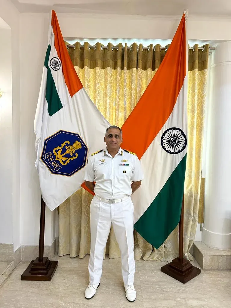 Captain Mahesh Khochare (Retd.) in Navy dress whites, the Naval ensign and the tricolour behind him