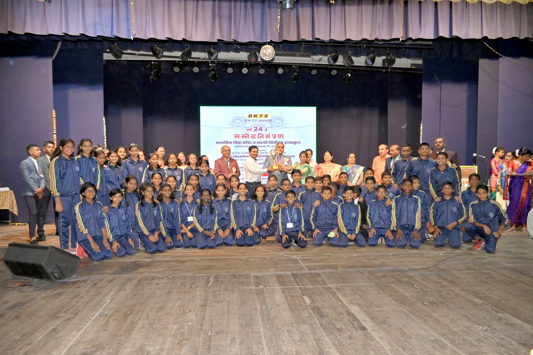 A large group of uniformed schoolchildren and guests photographed on stage