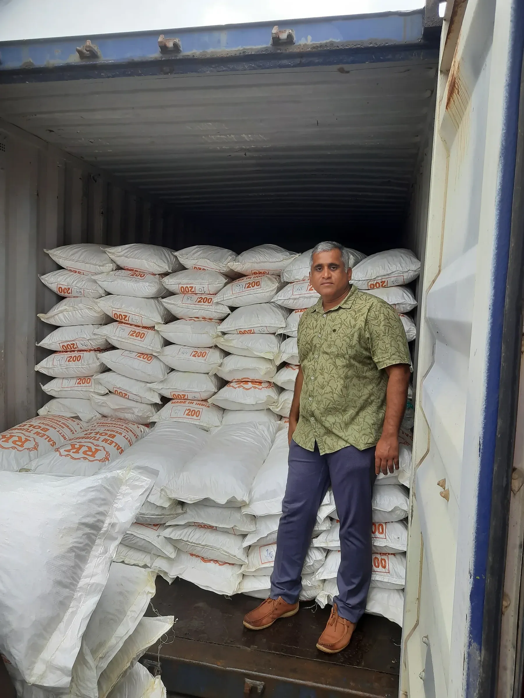 A man standing inside a part-loaded shipping container stacked with printed export sacks