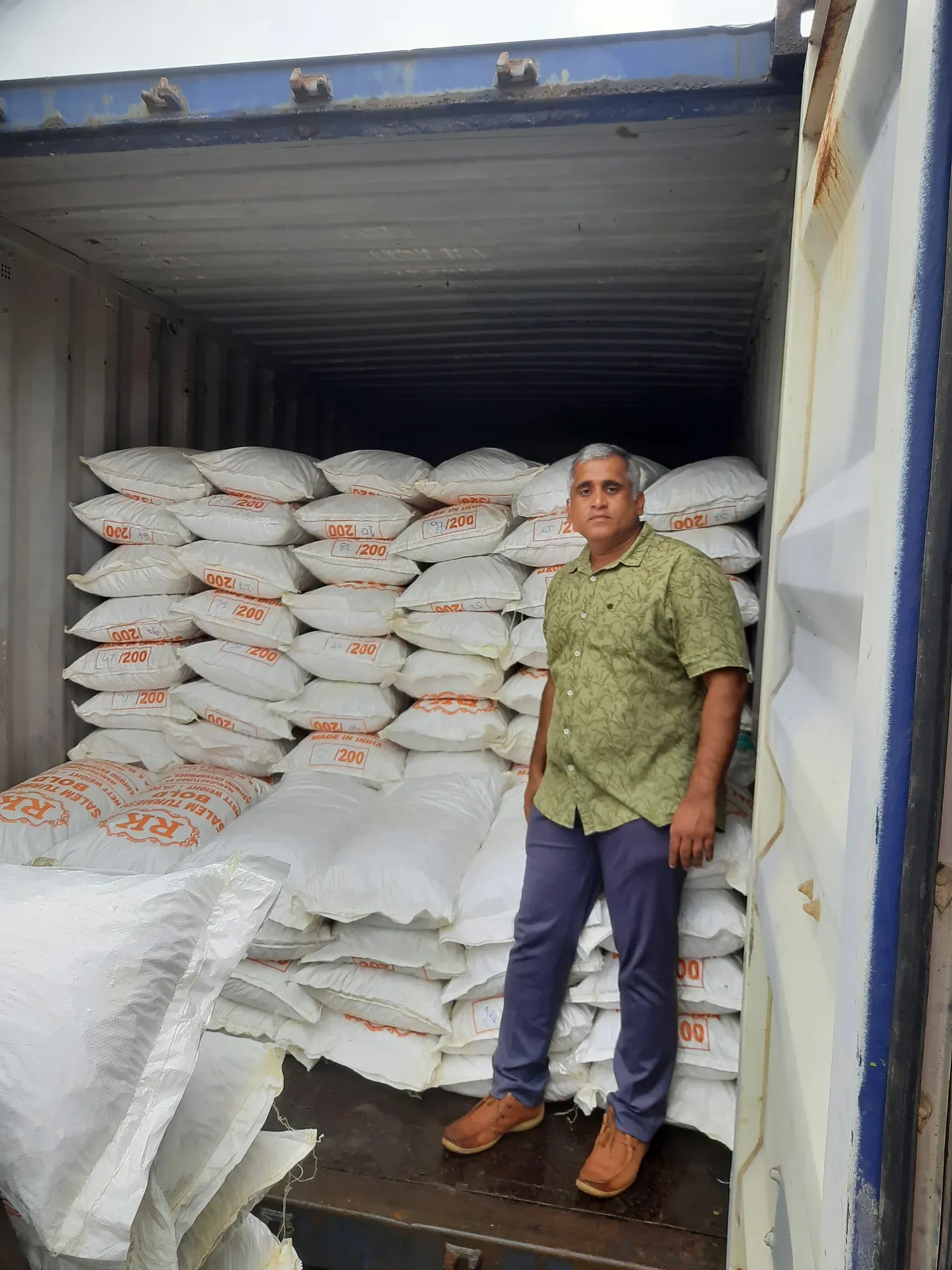 A man standing in front of sacks stacked to the roof inside a container bound for Malaysia