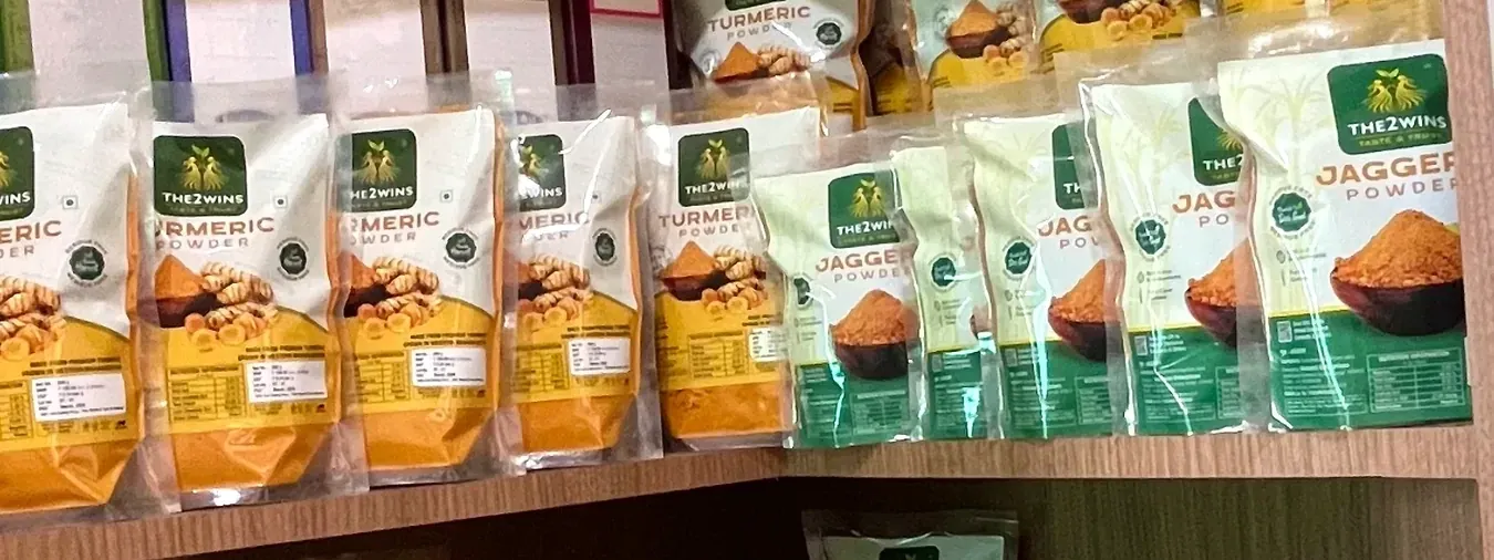 A shop shelf lined with THE2WINS turmeric powder and jaggery powder pouches