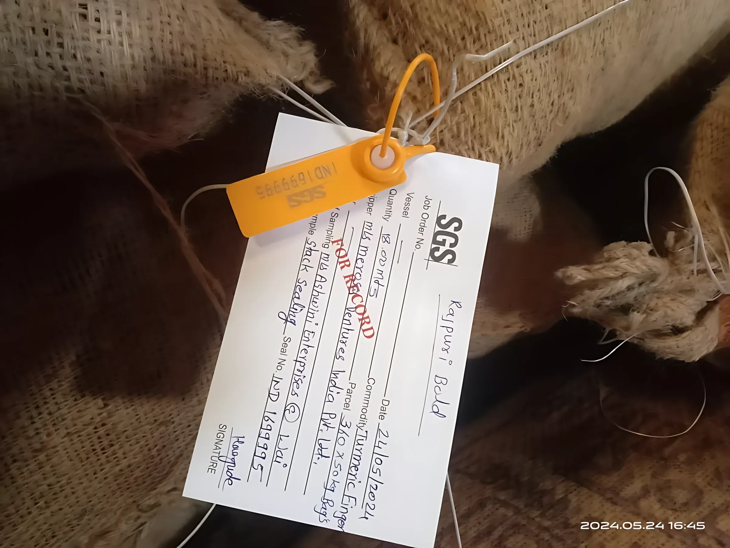 An SGS inspection tag and numbered orange seal fastened to a jute bag, recording the commodity and bag count